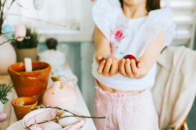 Pretty little Armenian girl helps with baking for Easter on veranda on sunny spring day decorated with flowers and Easter decor eggs cake and willow branches Easter family celebration