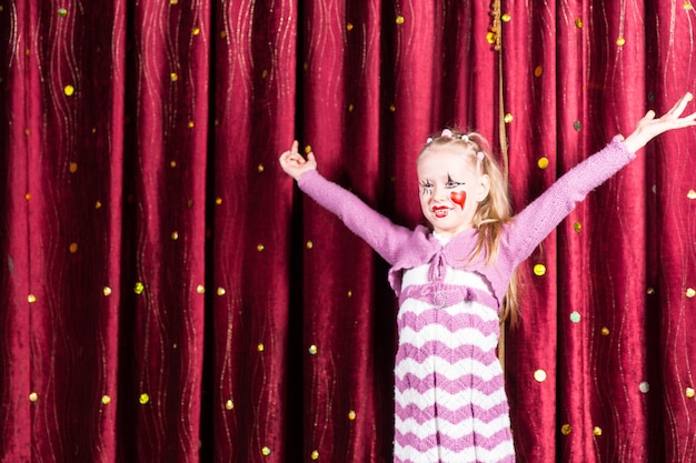 Pretty little blond girl in pantomime costume standing on stage playing to the audience with her arms outstretched and a big smile