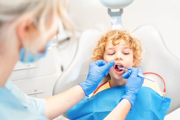 Pretty little boy in dental office, having his teeth checked by female dentist .