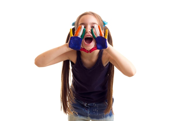 Pretty little girl in black shirt and jeans with two ponytails and colored hands shouting  in studio