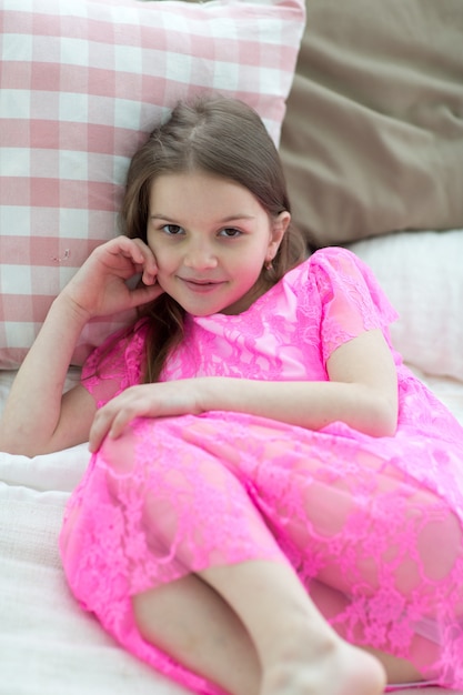 Pretty little girl in pink princess dress in bed with cushin