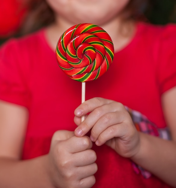 Pretty little girl in red dress holding a lollipop hard caramel in a hands.