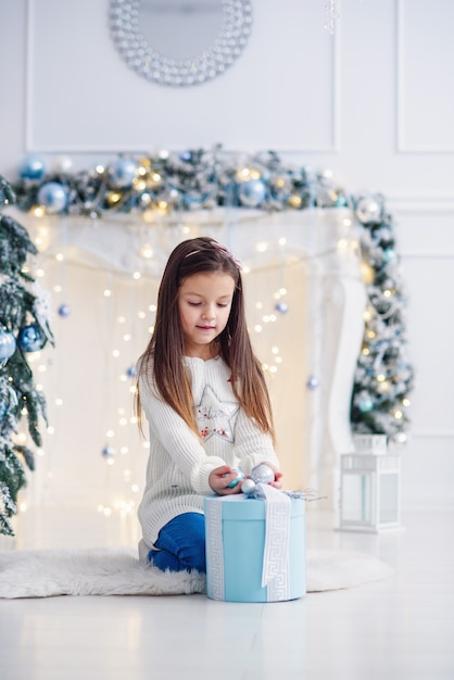 Pretty little girl sitting near Christmas tree indoors.