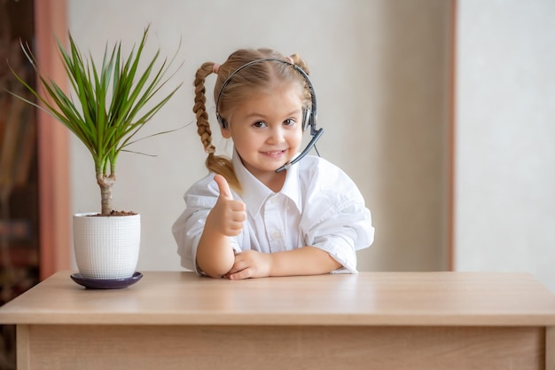 Pretty little girl sitting at table wearing headphones with mic looking at camera High quality photo