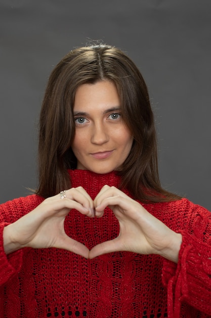 Pretty longhaired brunette girl making heart gesture finger looking at front