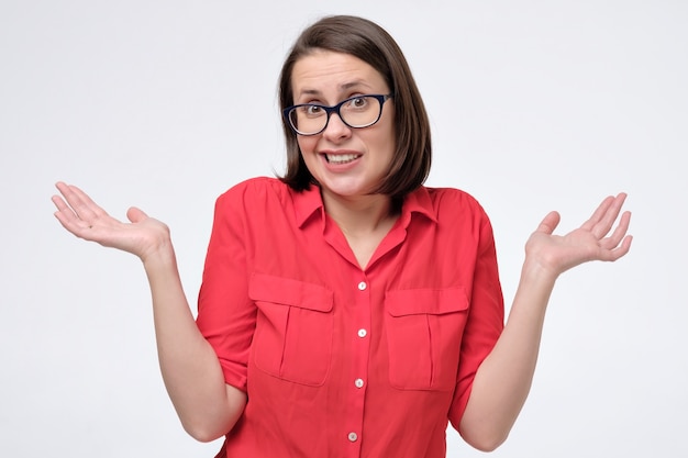 Pretty mature caucasian woman in red shirt and glasses shrugs shoulders