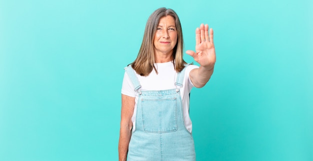 Pretty middle age woman looking serious showing open palm making stop gesture