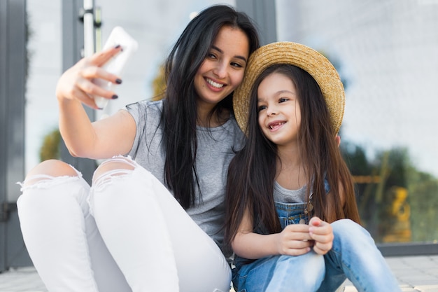 Pretty mother and little daughter make selfie photo by smartphone