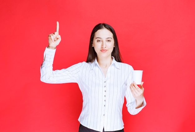 Pretty office employee posing with plastic cup of tea over red wall. 