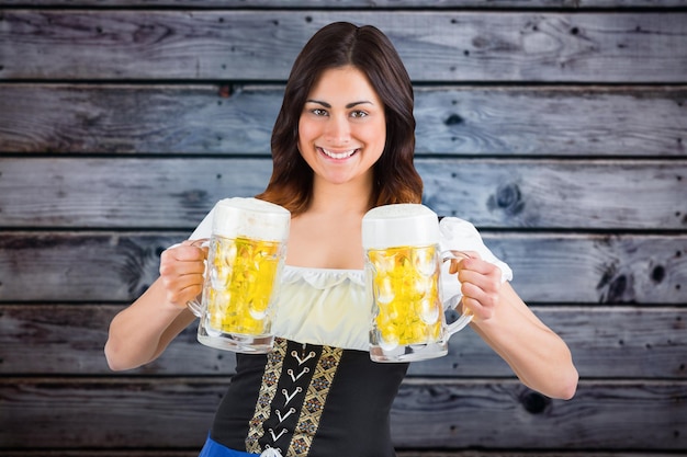 Pretty oktoberfest girl holding beer tankards against grey wooden planks