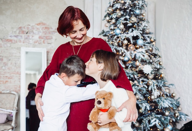 Pretty old lady with her grandchildren before a Christmas tree 