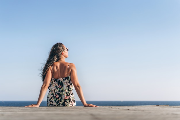 Pretty pan asian girl in dress sitting on the pier near sea.