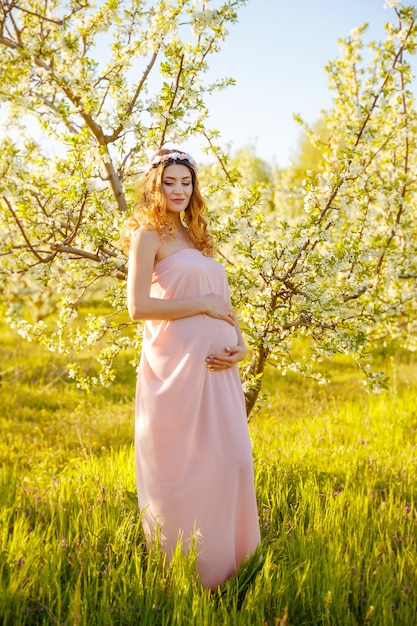 Pretty pregnant woman holds hands on belly in the spring garden