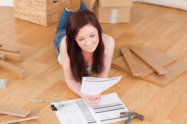 Photo pretty red-haired girl reading a manual before do-it-yourself while lying on the floor