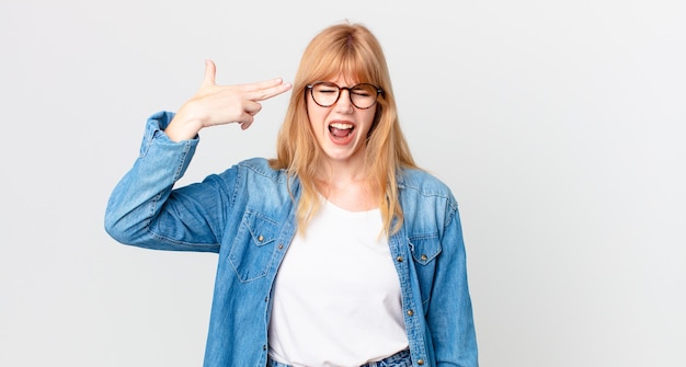 Pretty red head woman looking unhappy and stressed, suicide gesture making gun sign