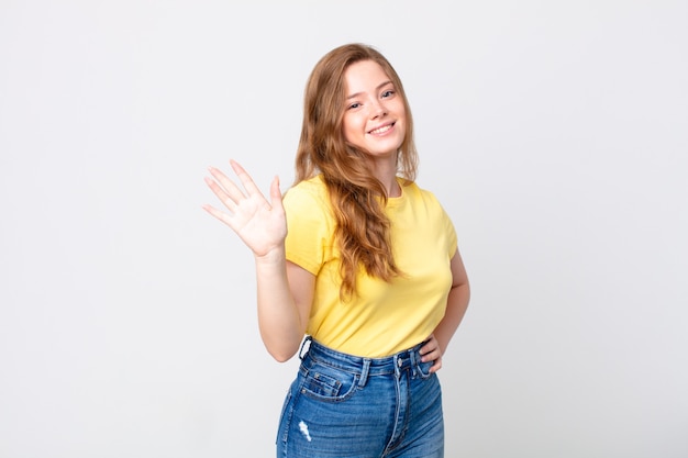 Pretty red head woman smiling happily, waving hand, welcoming and greeting you