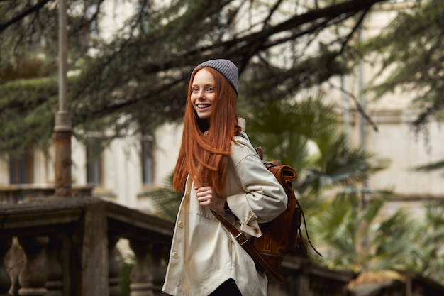 Pretty redhead woman in coat in search of beautiful historical place looking at side at attractions beautiful female spend time outdoors walking alone standing on historical balcony