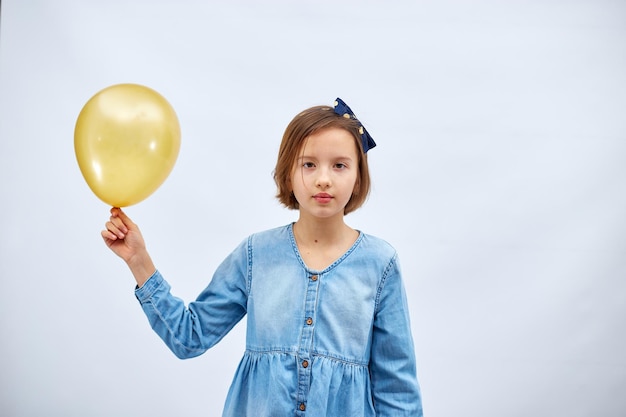 Pretty sad little girl in casual denim dress hold in hand yellow balloon