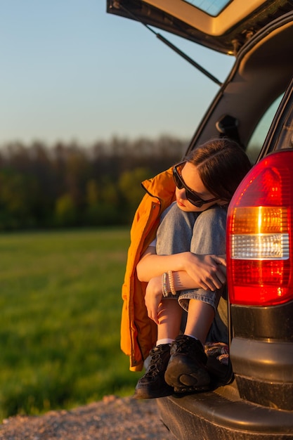 Pretty sad teenage girl with sun glasses sitting alone in a car trunk