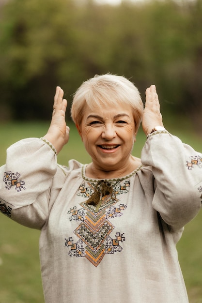 Pretty senior woman in traditional ukrainian embroidered shirt on park background