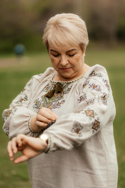 Pretty senior woman in traditional ukrainian embroidered shirt on park background