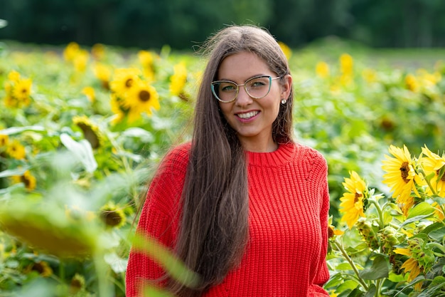 Pretty sensual young brunette in a field of sunflowers in a red sweater happy woman outdoors