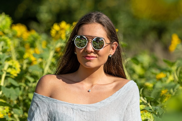 Pretty sensual young brunette in sunglasses in a field of blooming sunflowers young woman portrait