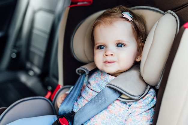 Pretty small child, girl  with blue eyes sits in the automobile armchair, fastened by seat belts.