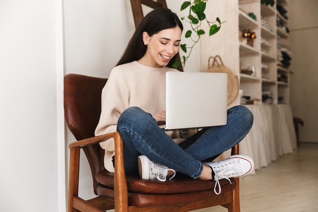 pretty smart woman resting in apartment and working on laptop computer while sitting on chair