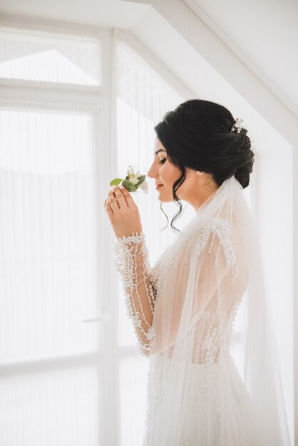 Pretty smiling Caucasian bride smelling a tender buttonhole bouquet