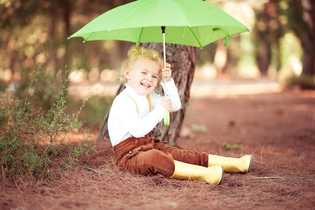 Pretty smiling kid girl holding umbrella having fun in autumn park outdoor