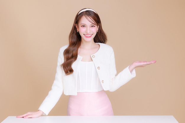 Pretty smiling young office Asian business entrepreneur smile showing open hand palm standing on isolated beige background concept for commercial advertising