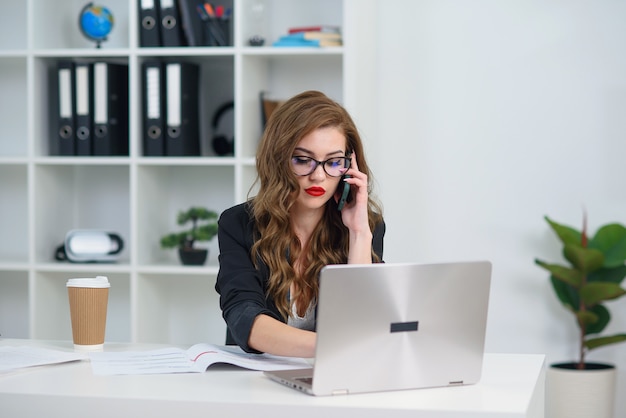 Pretty stylish business woman in glasses having business phone conversation at office.