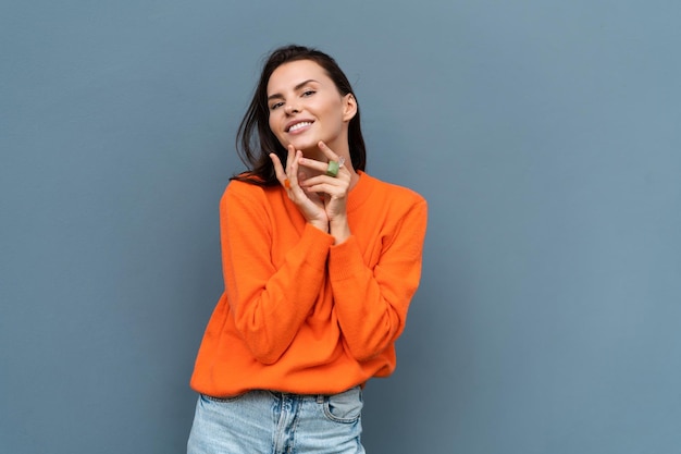 Pretty stylish woman in orange sweater posing on blue wall background outdoor wearing colorful rings accessories on fingers cute jewelry close shots