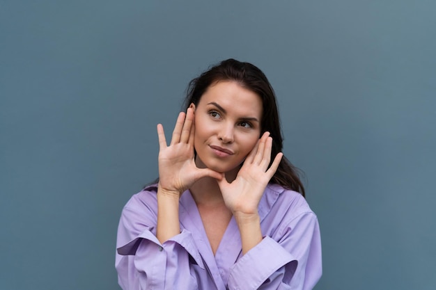 Pretty stylish woman in purple shirt posing on blue wall background long dark beautiful hair natural makeup soft skin