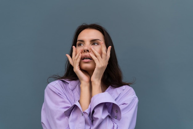 Pretty stylish woman in purple shirt posing on blue wall background long dark beautiful hair natural makeup soft skin