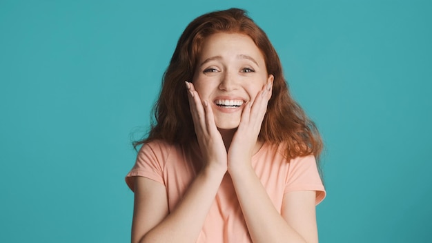 Pretty surprised emotional redhead girl happily posing on camera over over background Rejoicing expression