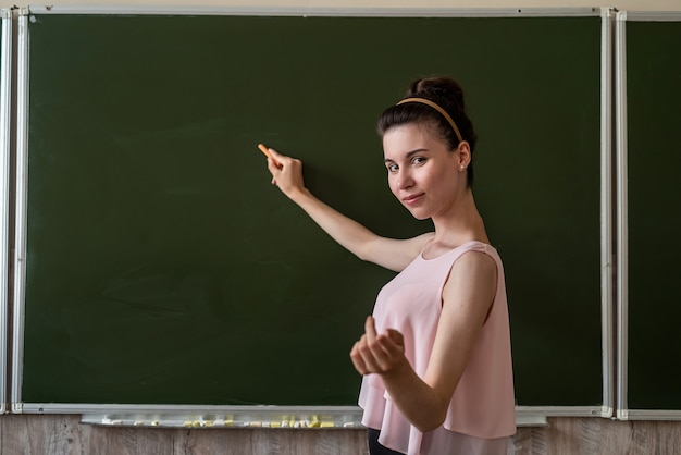 Photo pretty teacher explain new lesson near the empty school blackboard, copy space for text