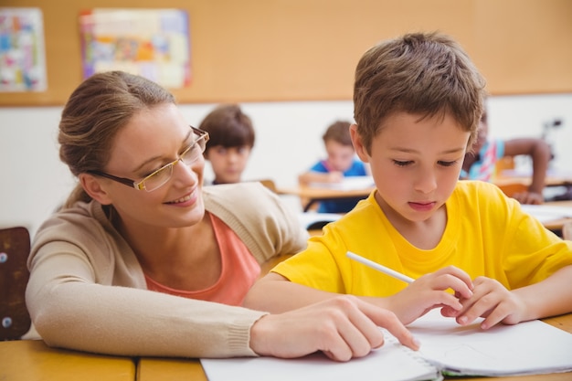 Pretty teacher helping pupil in classroom