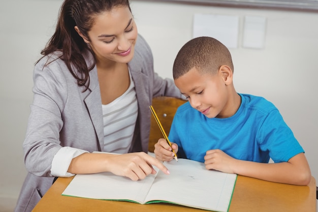 Pretty teacher helping pupil at his desk 