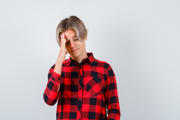 Pretty teen boy suffering from migraine in checked shirt and looking bothered , front view.