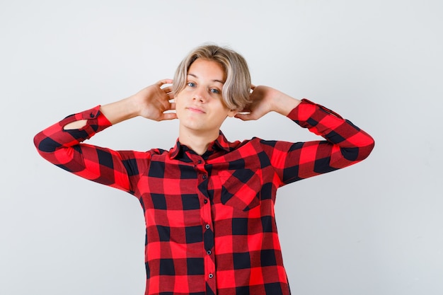 Pretty teen boy with hands behind head in checked shirt and looking relaxed. front view.