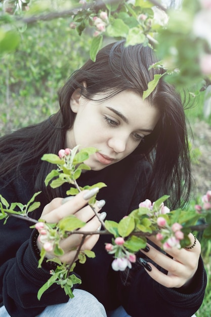 Pretty teen girl are posing in garden near blossom apple tree with pink flowers