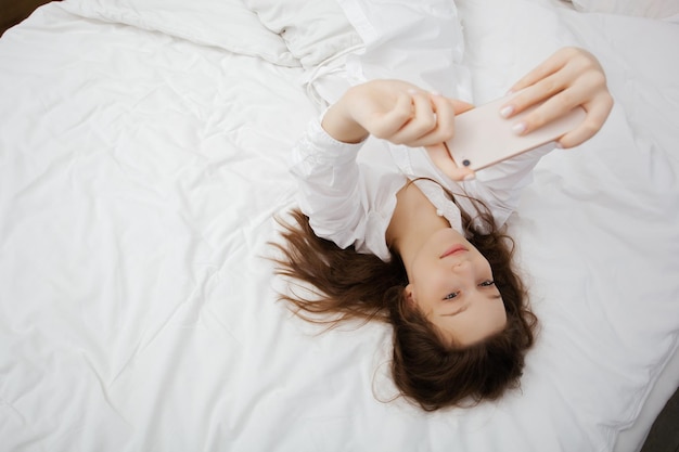 Pretty teen girl makes selfie on her smartphone while laying in a bedroom