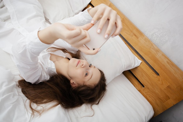 Pretty teen girl makes selfie on her smartphone while laying in a bedroom