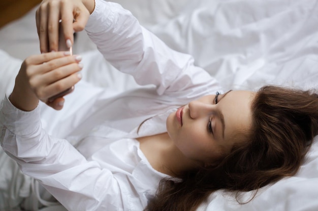 Pretty teen girl makes selfie on her smartphone while laying in a bedroom