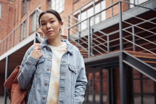 Pretty teenage girl in denim jacket holding backpack on shoulder