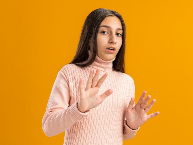 Pretty teenage girl looking at front doing refusal gesture with open mouth isolated on orange wall