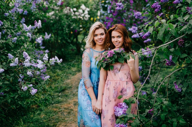 Pretty, tender and cheerful twins sisters in beautiful dresses posing together in summer sunny park.