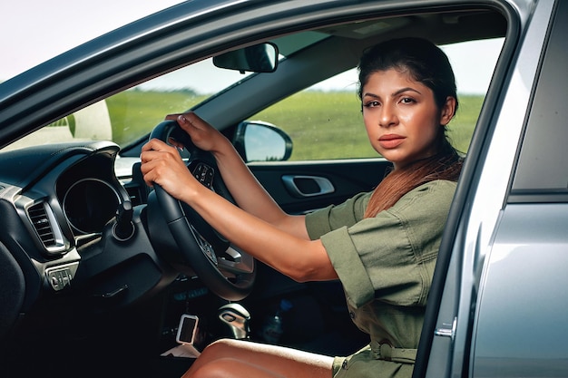 Pretty thin lady is sitting in the car and holding the steering wheel, portriat